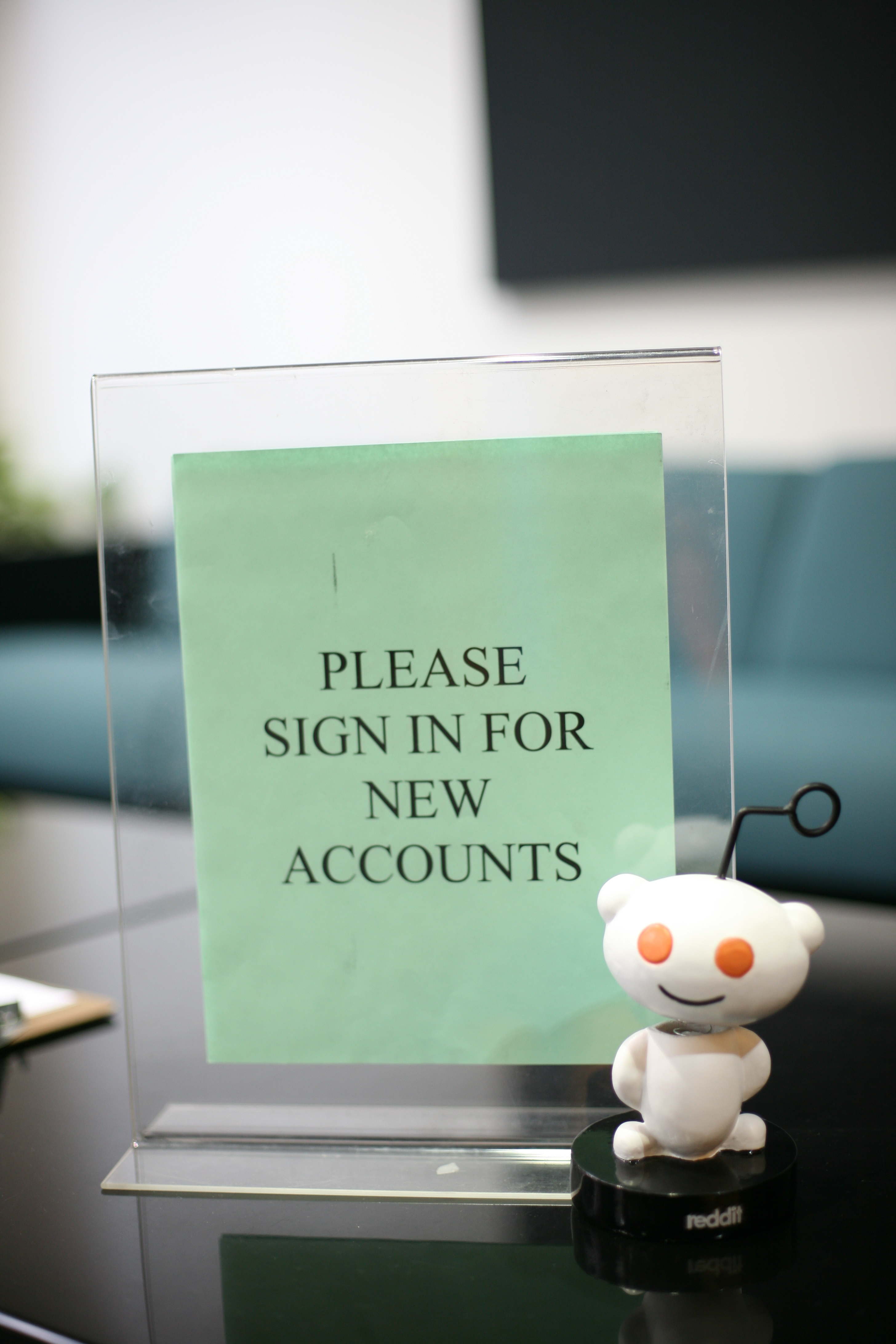 Reddit alien figurine beside a tabletop sign reading 'Please sign in for new accounts'